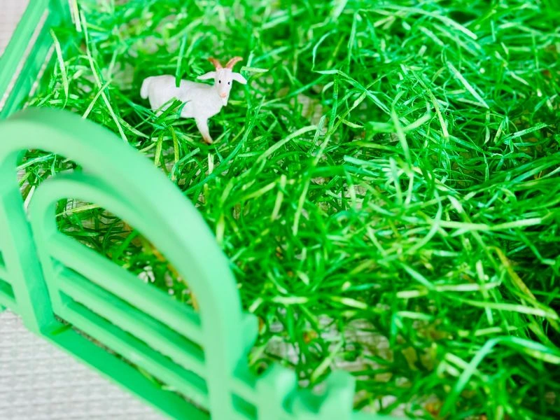 Miniaturziege steht in grünem Ostergras innerhalb eines dekorativen Zauns aus dem 3D-Drucker.