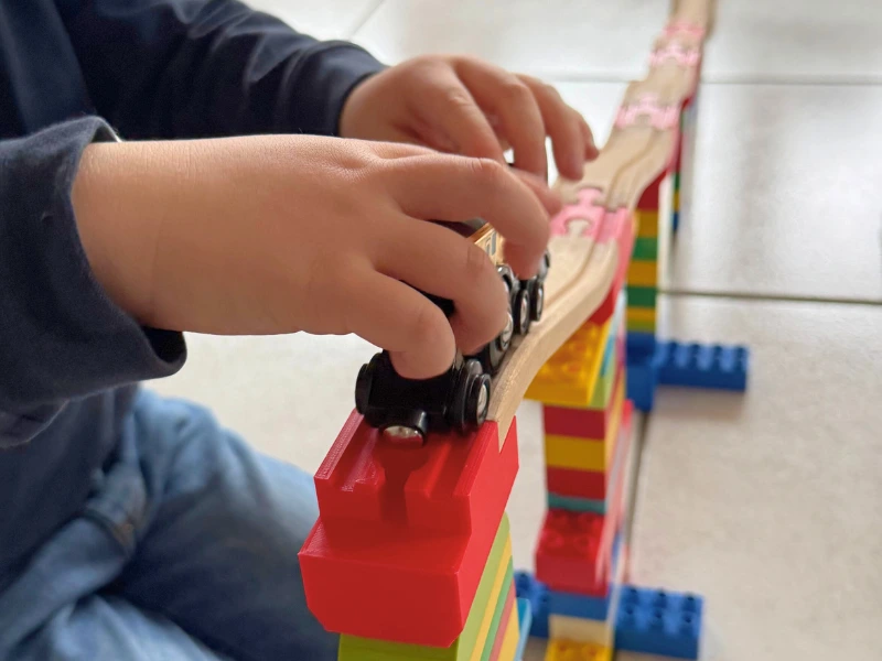 Kind spielt mit Zug auf Holzschienen, gestützt von 3D-gedruckten Duplo-Adaptern