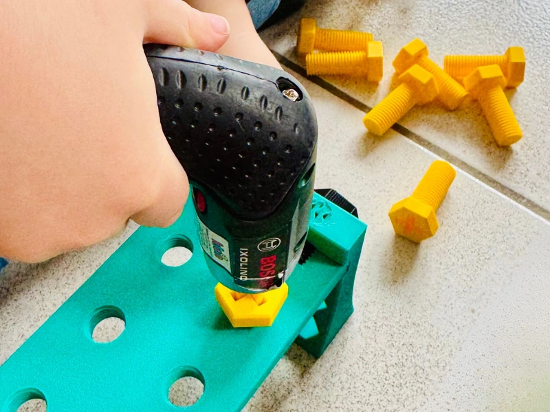 3D-Druck Schraube im Einsatz mit Bosch Kinder-Werkzeug Kind benutzt Bosch Kinder-Akkuschrauber mit 3D-gedruckter Schraube auf Werkbank