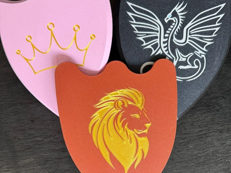Drei farbenfrohe 3D-gedruckte Ritterschilder für Kinder – pink mit Krone, schwarz mit Drache, rot mit Löwenmotiv