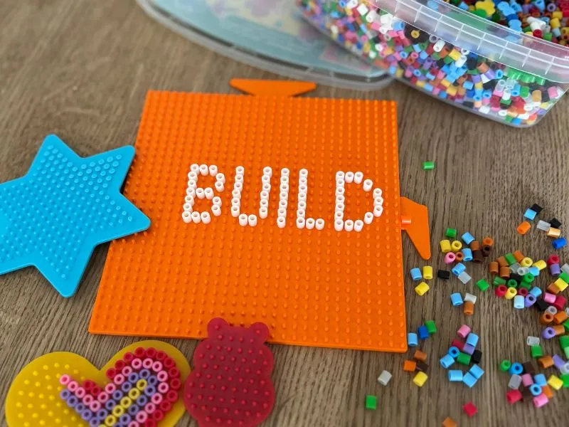 3D-gedruckte modulare Hama-Pegboards für Bügelperlen in Orange, Blau und Gelb mit Schriftzug BUILD.
