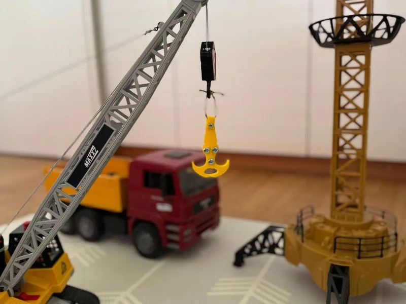 3D-gedruckter Schwerkraft-Haken an einem Spielkran mit Baustellen-LKW im Hintergrund