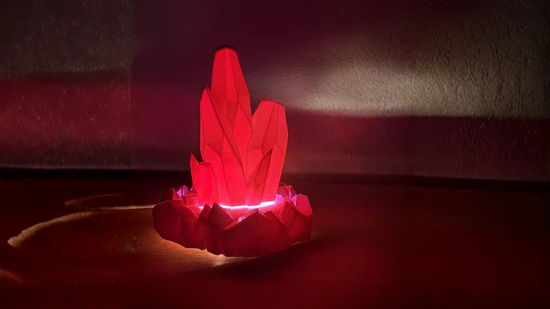 Rot leuchtender 3D-gedruckter Kristall auf Holzuntergrund mit warmem, atmosphärischem Licht.