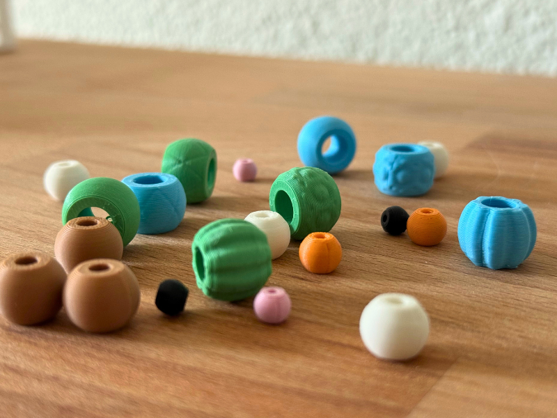 Bunte, 3D-gedruckte Bastelperlen in verschiedenen Farben und Formen liegen auf einem Holztisch.