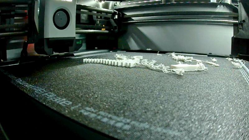 3D-Druck schlägt fehl: Der erste Layer haftet nicht auf der Druckplatte, mehrere lose Filamentfäden und verformte Druckreste liegen auf dem Bambu-Lab-Druckbett.