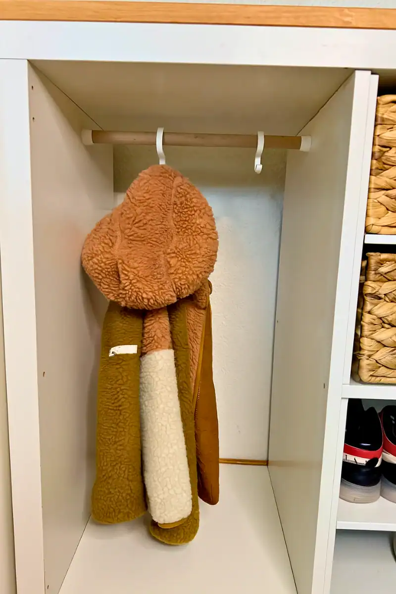 Kinder-Garderobe aus einem weißen IKEA-Kallax-Regal mit Holzabdeckung, eingebauter Kleiderstange und 3D-gedruckten S-Haken.