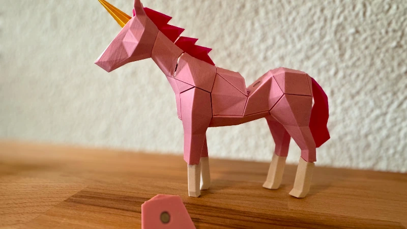Einhorn aus dem 3D-Drucker – magisch, modern und kindgerecht 3D-gedrucktes rosa Einhorn mit goldenem Horn und roter Mähne auf Holzuntergrund, inspiriert von einem Low-Poly-Design.