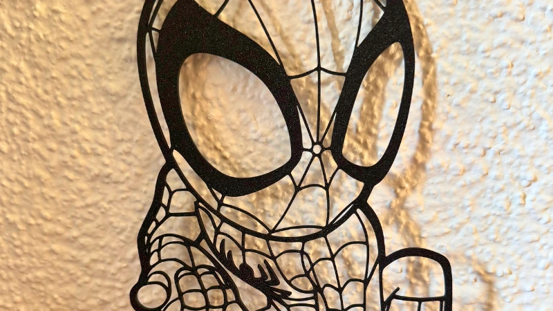 Schwarze, filigrane 3D-gedruckte Spidey-Wanddeko im Comicstil, montiert vor einer hellen strukturierten Wand.