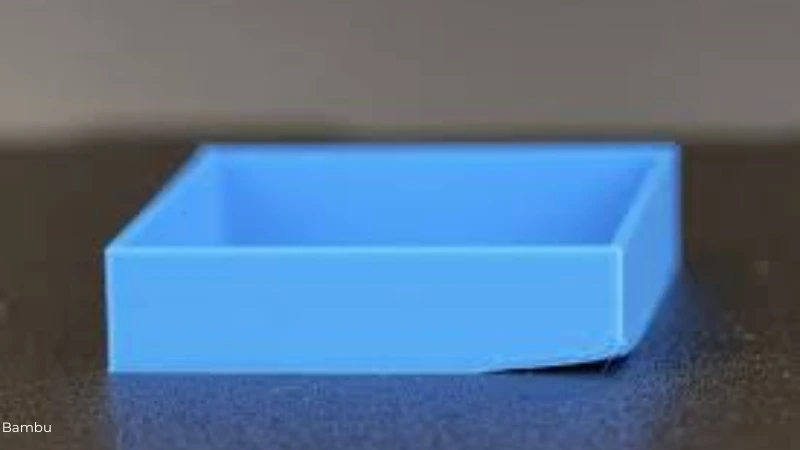 Blau gedruckte 3D-Box mit angehobener Ecke, die sich vom Druckbett löst – ein typisches Beispiel für Warping beim 3D-Druck.